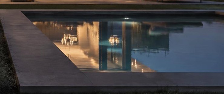 A pool reflecting the warm lights of the house behind it